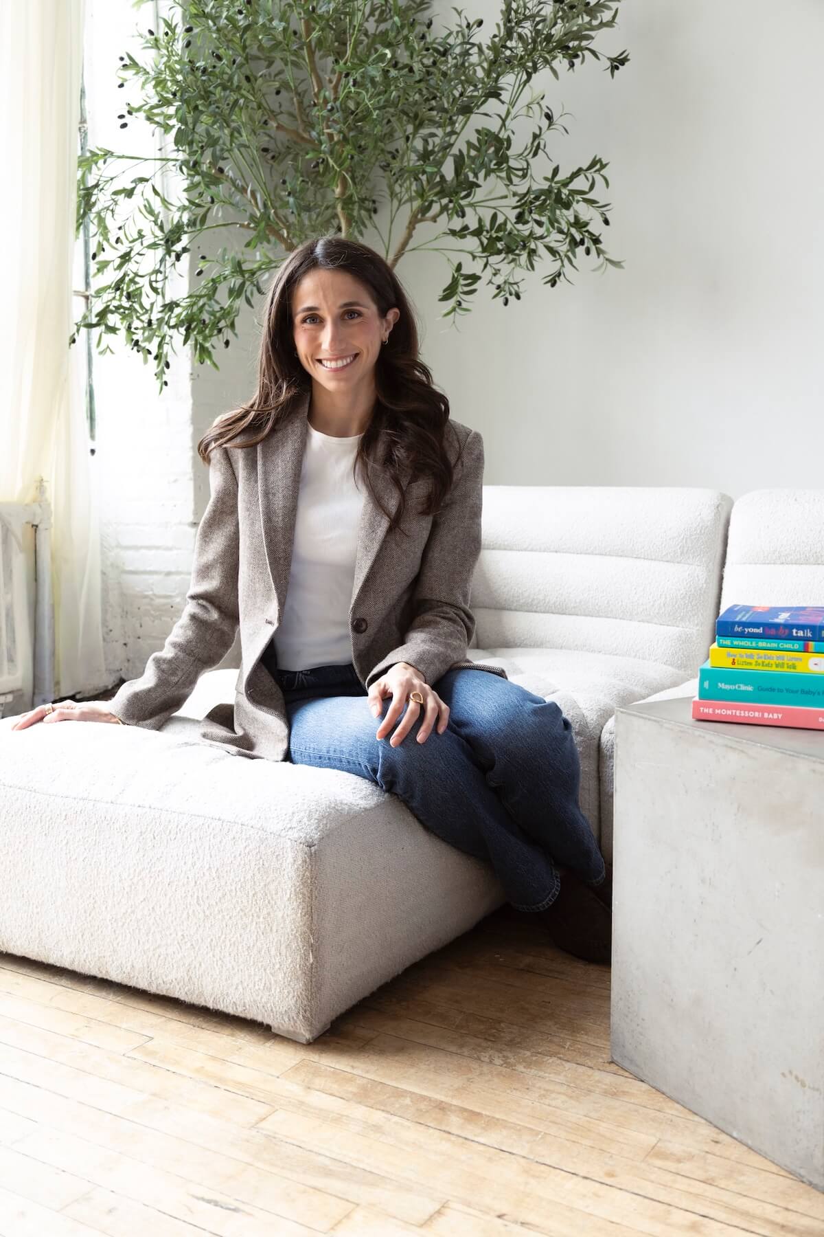 Kathryn Ressa, smiling, sitting on a light sofa, with books on the side of the image.